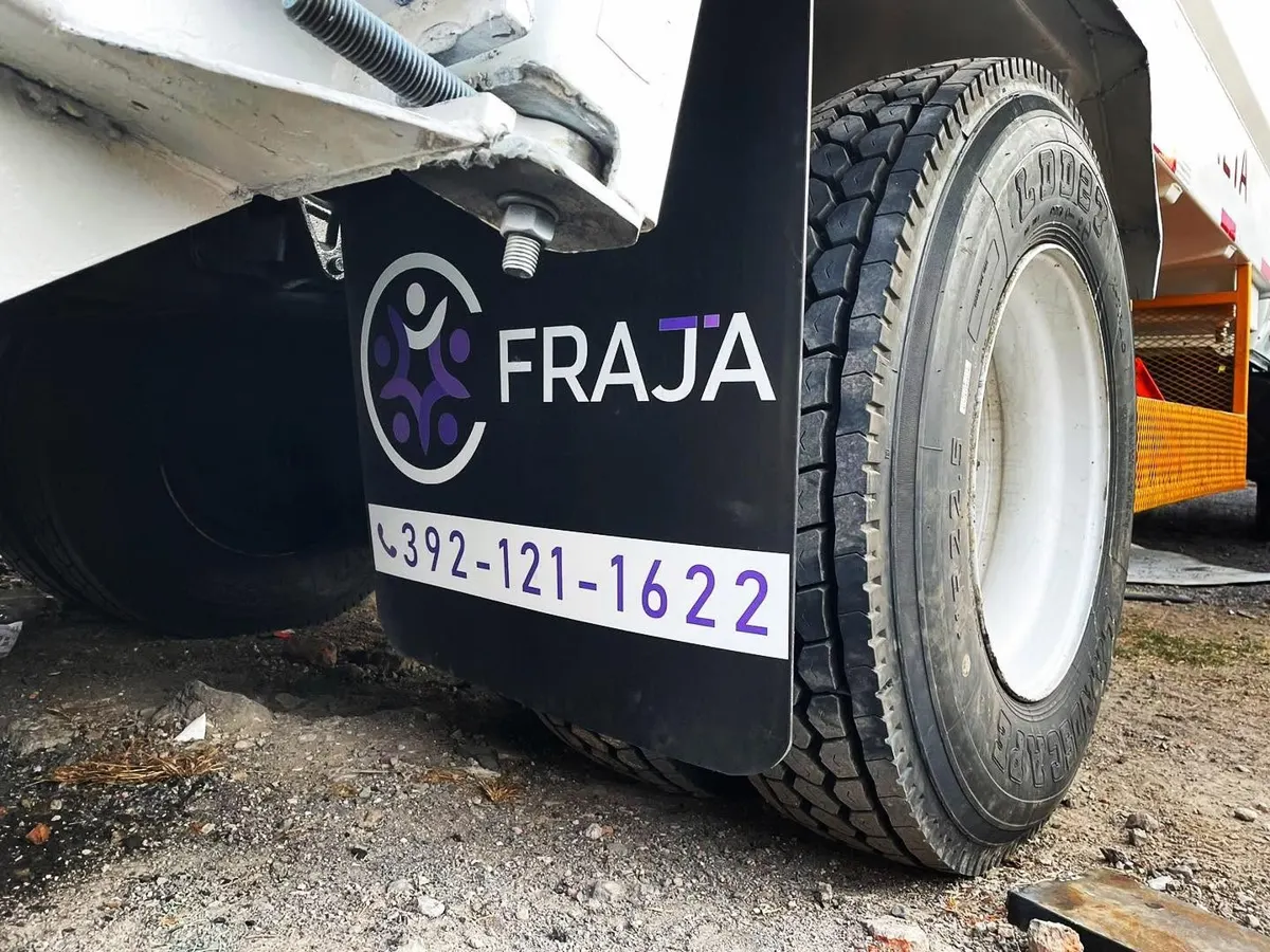 Lodera negra instalada detrás de la llanta trasera de un camión, con logotipo morado y número telefónico en blanco