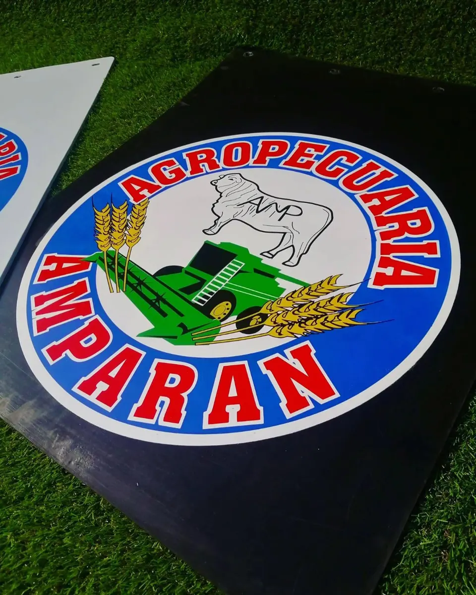 Lodera negra con emblema circular azul y rojo de una empresa agropecuaria, con ilustración de ganado, espigas y tractor