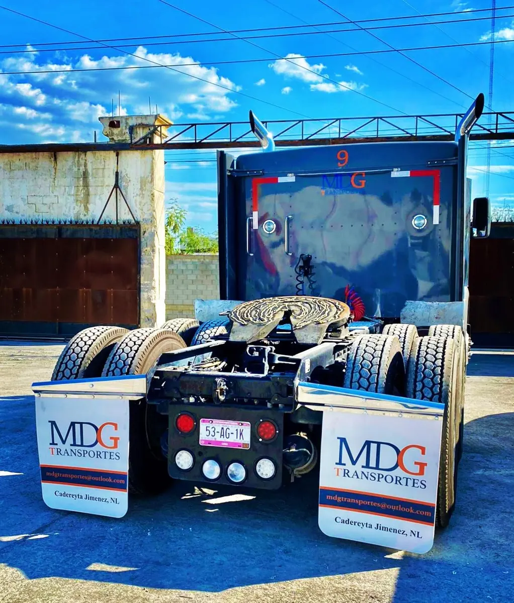 Tractocamión azul visto desde atrás en un patio, con dos loderas blancas personalizadas instaladas con el logotipo de una transportista