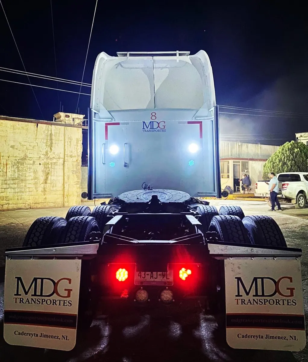 Tractocamión de noche visto desde atrás con un par de loderas blancas personalizadas con el logotipo de una empresa transportista